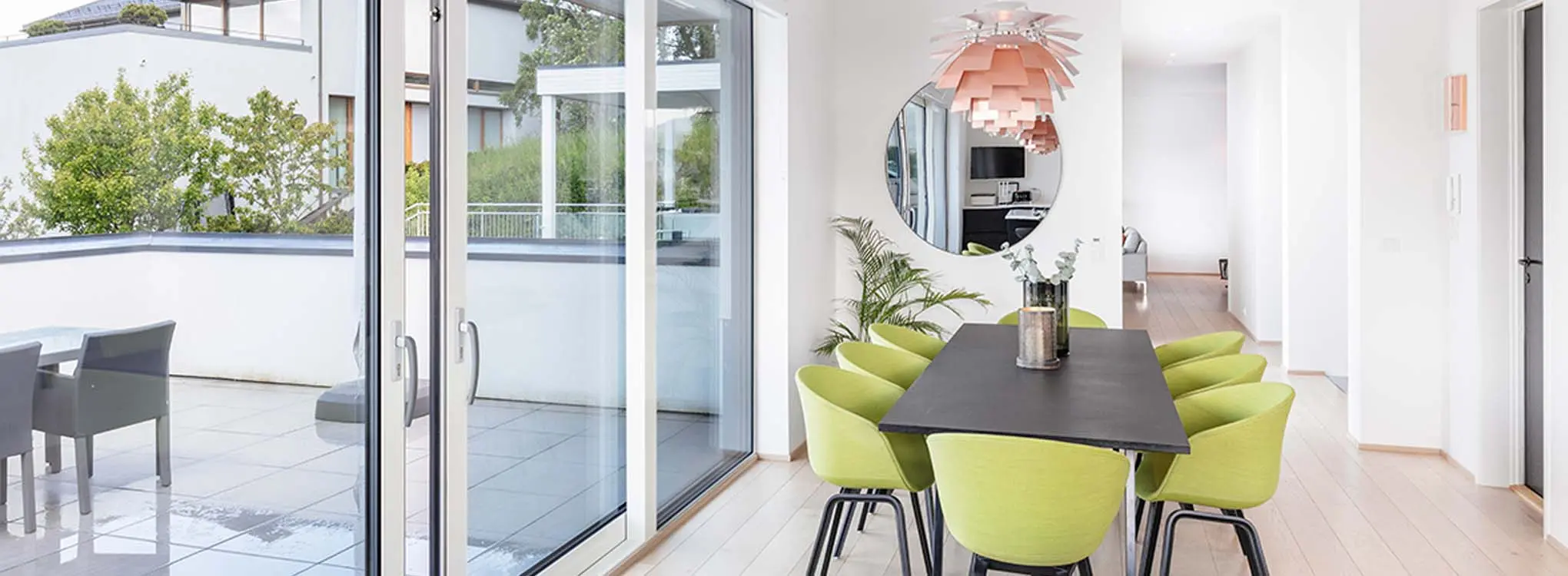 minimalistisk stue med grønne spisestoler og en åpen verandadør i bakgrunnen