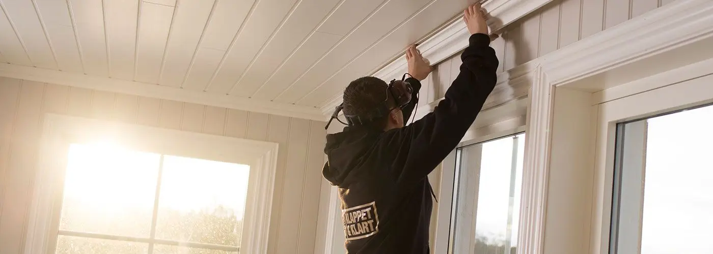 snekker med XL-BYGG-genser monterer taklister i en stue