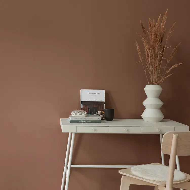 hvitt skrivebord og stol i skandinavisk stil står mot en rustfarget vegg.